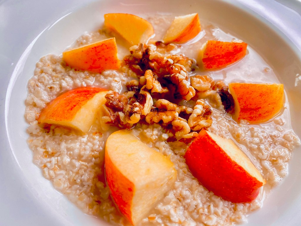 Bowl of oatmeal topped with black walnuts and sliced apples.